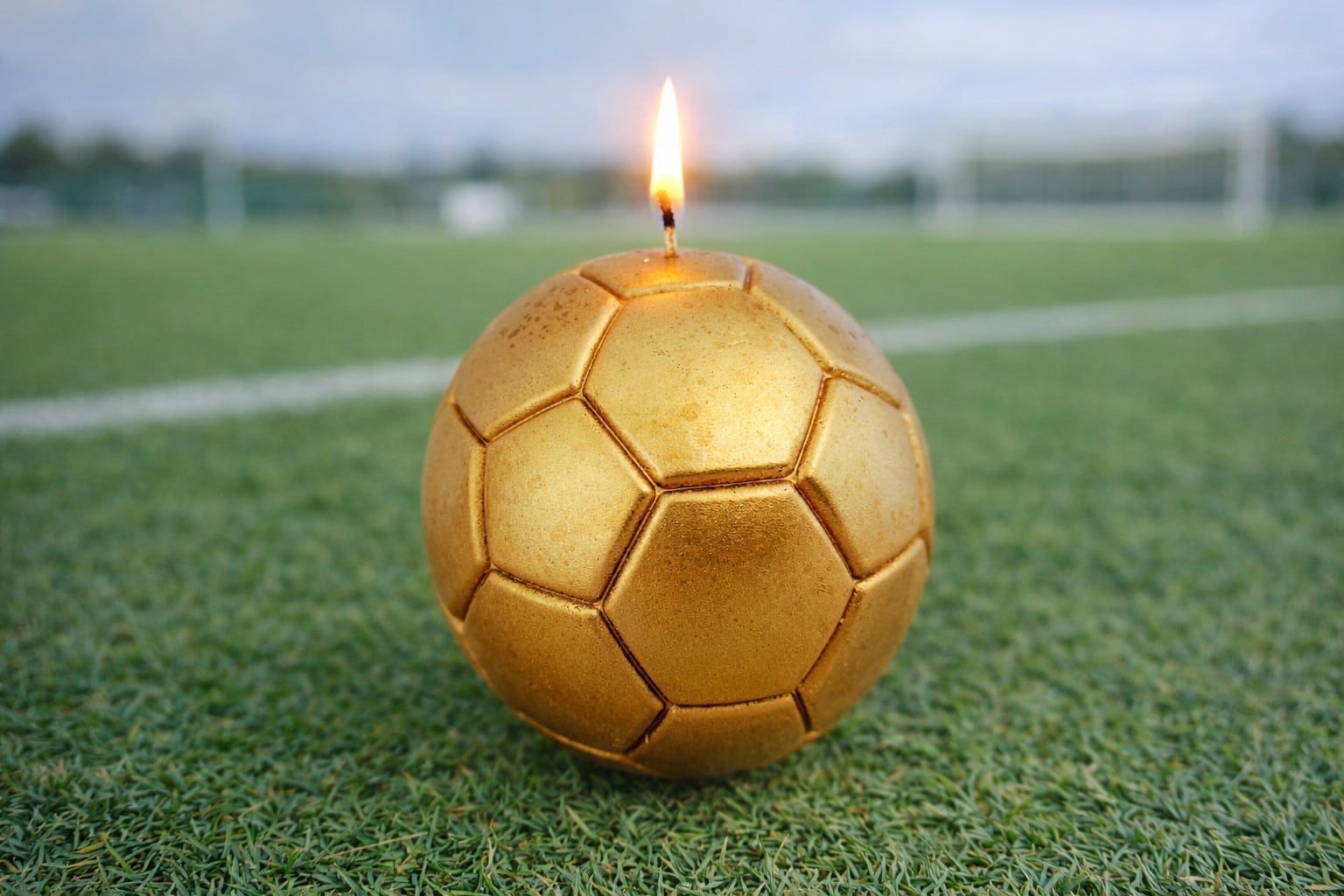 Bougie ballon de football dorée allumée de 8 cm posée sur un terrain de foot