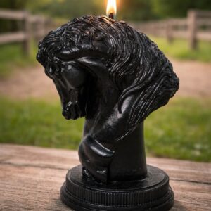 Bougie tête de cheval noire artisanale allumée sur fond de haras avec clôture et nature