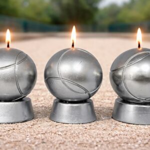 Trois bougies en forme de boules de pétanque métalliques allumées sur terrain de pétanque